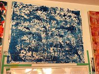 Front view of the abstract painting predominantly in blue and white colors, showing the textured composition against a wall among other artworks.