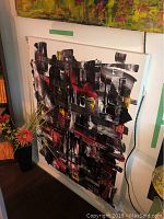 Front view of unframed abstract painting with bold black, white, red, and yellow brush strokes leaning against wall.