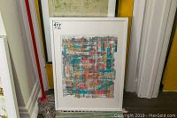 Full view of framed painting leaning against wall on patterned carpet with mop beside it