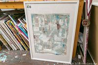 Framed abstract art piece by Alex Hare propped against a table, showing its size and color details.