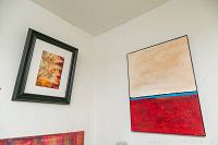 Larger abstract unframed painting by Alex Hare featuring red and beige color blocks divided by a blue line, hanging on a wall.