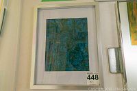 Framed abstract art piece by Alex Hare shown hanging on a wall. The artwork is framed in a white frame and depicts an abstract composition in blue and green tones with textured appearance.