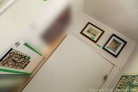 Framed and unframed wall art in a corner showing two pieces hung, and a third leaning against the wall with an auction lot label nearby