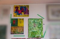 Overall view of three abstract paintings taped to a wall showing their sizes and colors.