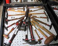 Top-down view of 18 vintage hammers arranged on peg board inside framed case showing a variety of handle types and hammer heads.