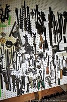 Various hand braces, auger bits, wrenches, spanners and pliers hanging on white pegboard
