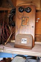 Front view of large wooden vintage wall telephone with black bells and crank handle on the side.