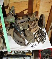 Five antique clothes irons of various styles with wooden handles and metal bodies, accompanied by several decorative iron rests on a table.