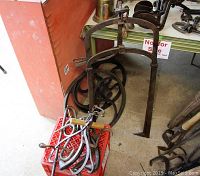 Overview photo of cast iron ice hooks, hay fork, lumber hooks in front of a red milk crate (not included for sale), with cast iron pulley and wheel behind.