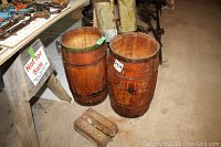 Two small vintage wooden nail barrels placed on the floor, showing varnished wood and metal bands, with a cast iron brush attachment labeled Comfort in front of barrels.