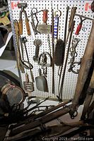 Photo of horse grooming tools and tack hanging on pegboard including clippers, brushes, and metal stirrups