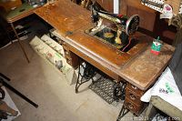 Wooden sewing table with Singer sewing machine built inside, visible wear and included sewing oil can on table surface