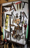 Photo showing pegboard with hanging wood carving knives, carpenter squares, spirit levels, wire cutters, and a padlock.