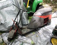 Side view of vintage motorbike showing body, seat, and handlebars with gray and orange/red paint and rust.