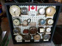Full front view of 16 vintage alarm clocks mounted on black pegboard display with Canadian flag and label showing collection of 332 clocks.