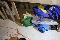 Photo showing the camping equipment including tarps, portable bed frame in a carrying bag, and Hershey floats arranged under wooden shelving.