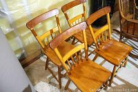 Four solid wood dining chairs arranged in two rows, showing the front and side views with visible minor wear on seats and backs.