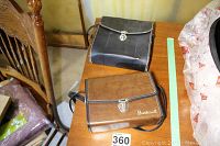 Two carrying cases on a wooden table, one brown with Bushnell branding and one black Skyline case.