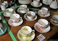 View of multiple tea cup and saucer sets arranged on a wooden surface, featuring floral designs