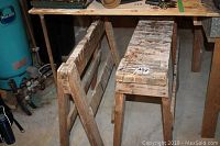 Front angle showing two wooden saw horses stacked under a workbench, paint drips and saw marks visible on surfaces.