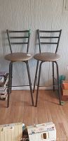 Front view of two metal swivel bar stools with padded seats and back slats, placed side by side.