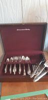 Open wooden chest displaying 1847 Rogers Bros IS silver plate flatware with maroon velvet lining.