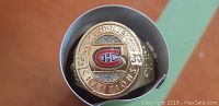 Close up photo of a gold-toned Montreal Canadiens commemorative Stanley Cup ring with team logo and 'Stanley Cup Champions' text, displayed in a round gray case.