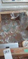 Multiple clear glasses and bowls in cardboard box featuring a variety of sizes and styles, including stemmed and tumblers