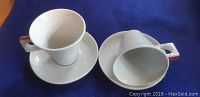 Two white porcelain Nescafe espresso cups, one upright and one upside down, showing shape and handle detail