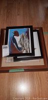 Stack of five framed bird artworks with visible framed picture of a bird with red head on wood.