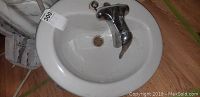 Top view of the white oval ceramic sink with chrome faucet attached, showing the basin and faucet overall condition.