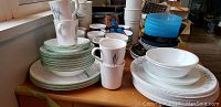 Photo showing stacked Corel ceramic dishes and mugs on wooden table