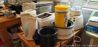 Photo showing various kitchen appliances including a white 4-slice toaster, black and white crockpots, and a canister on top.
