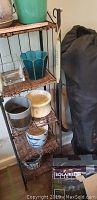Wrought iron and wicker shelving with multiple ceramic pots and solar lights visible beside a black camping chair bag.