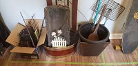 Photo showing brown garden border fencing roll, metal floral and butterfly garden stakes, white wooden picket fence decoration with daisy flowers placed inside the fencing roll, metal garden edging container, and plastic gardening pots.