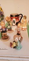 All five items arranged together showing four Hummel figurines and one kilt mug