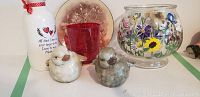 White and gray ceramic bird-shaped candle holders with hollow cavity for candles, displayed alongside a red glass votive holder, signed hand-painted floral enamel bowl, and white decorative bottle with heart.