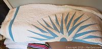 White blanket with blue-green starburst or leaf pattern spread out