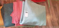 Four folded wool blankets stacked, in grey, pink, and light blue colors.