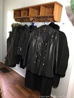 Photo showing a row of winter coats and leather jackets hung on wooden wall rack, including leather double-breasted jacket up front