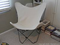 Front view of white canvas butterfly chair on black metal frame in room with books and window.