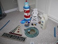 Wide view of all nautical decor items on carpet floor showing lighthouse birdhouse, seagull, mirror, small chair, small lighthouse cabinet, and the ship decor.
