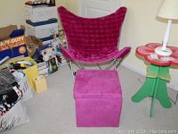 Butterfly chair and matching storage ottoman next to green flower-shaped side table and lamp in a room.