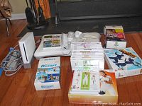 Photo shows white Nintendo Wii console, white Wii remotes, and multiple Wii game boxes arranged on floor.