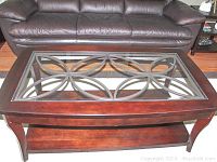 Front view showing the full coffee table with a dark wood frame, glass top with metal decorative insert, and lower shelf.