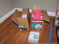 Four new Kidde smoke alarms and four Kidde carbon monoxide alarms in opened boxes on hardwood floor, with a boxed USB charger in front.