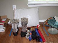 Khombu women's winter boots, six compact umbrellas with various colorful patterns, and a large white body pillow arranged on a hardwood floor.
