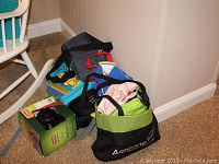 Photo showing a grouping of several used bags in various colors alongside a new Coleman camping ceiling fan and light combo box.