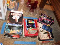 Photo showing a variety of used board games including Bridge, Sequence, Battleship, Tactics II, Star Wars Monopoly, Clue, and others stacked on the floor with some glass bottles visible behind