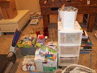 Wide view of the craft supplies spread out near a foosball table including the white three-drawer rolling storage container, boxes of supplies, colored pencils, glass vases, and various craft kits.